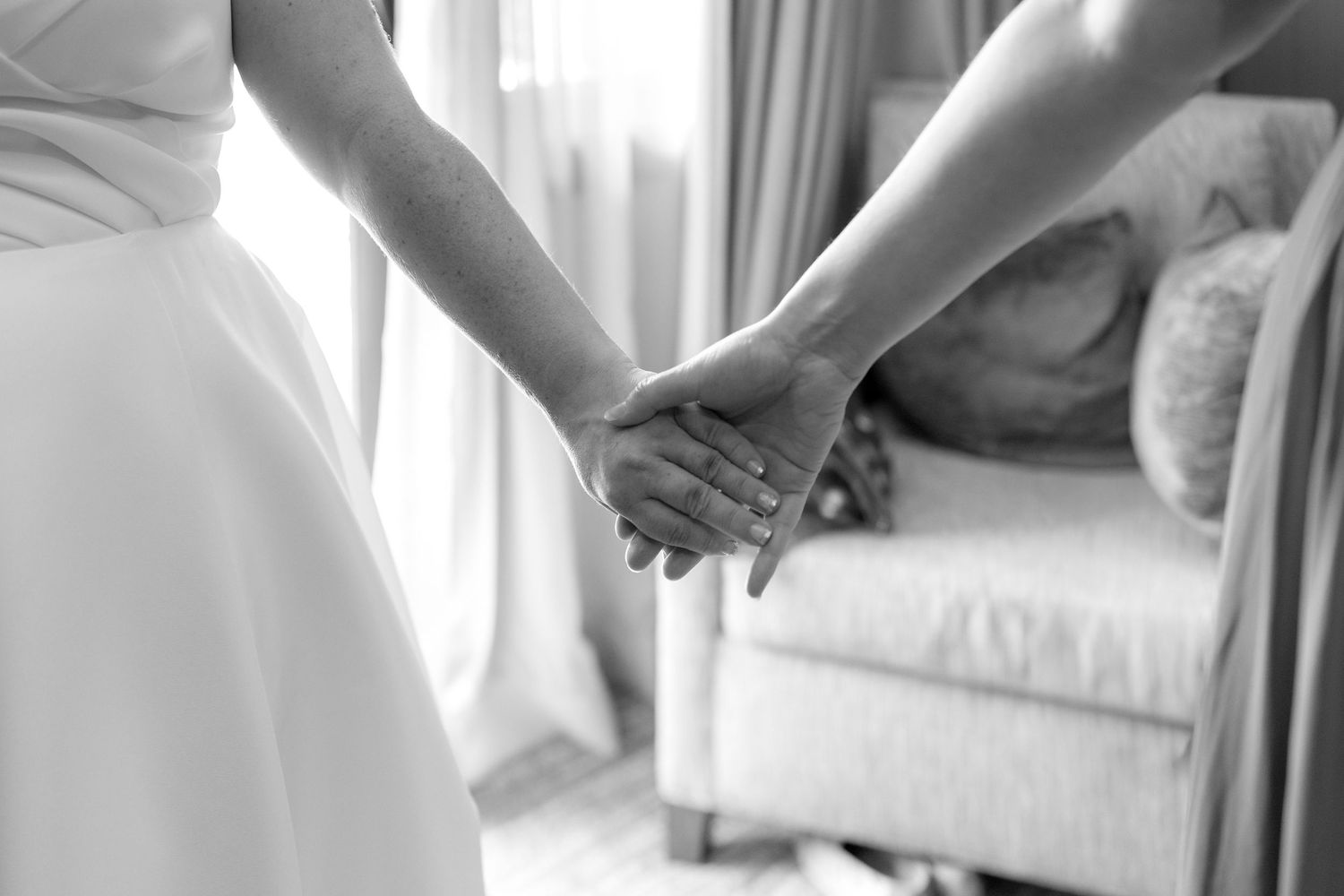 Detail shots of a bride's dress being buttoned up in a sunlit room.