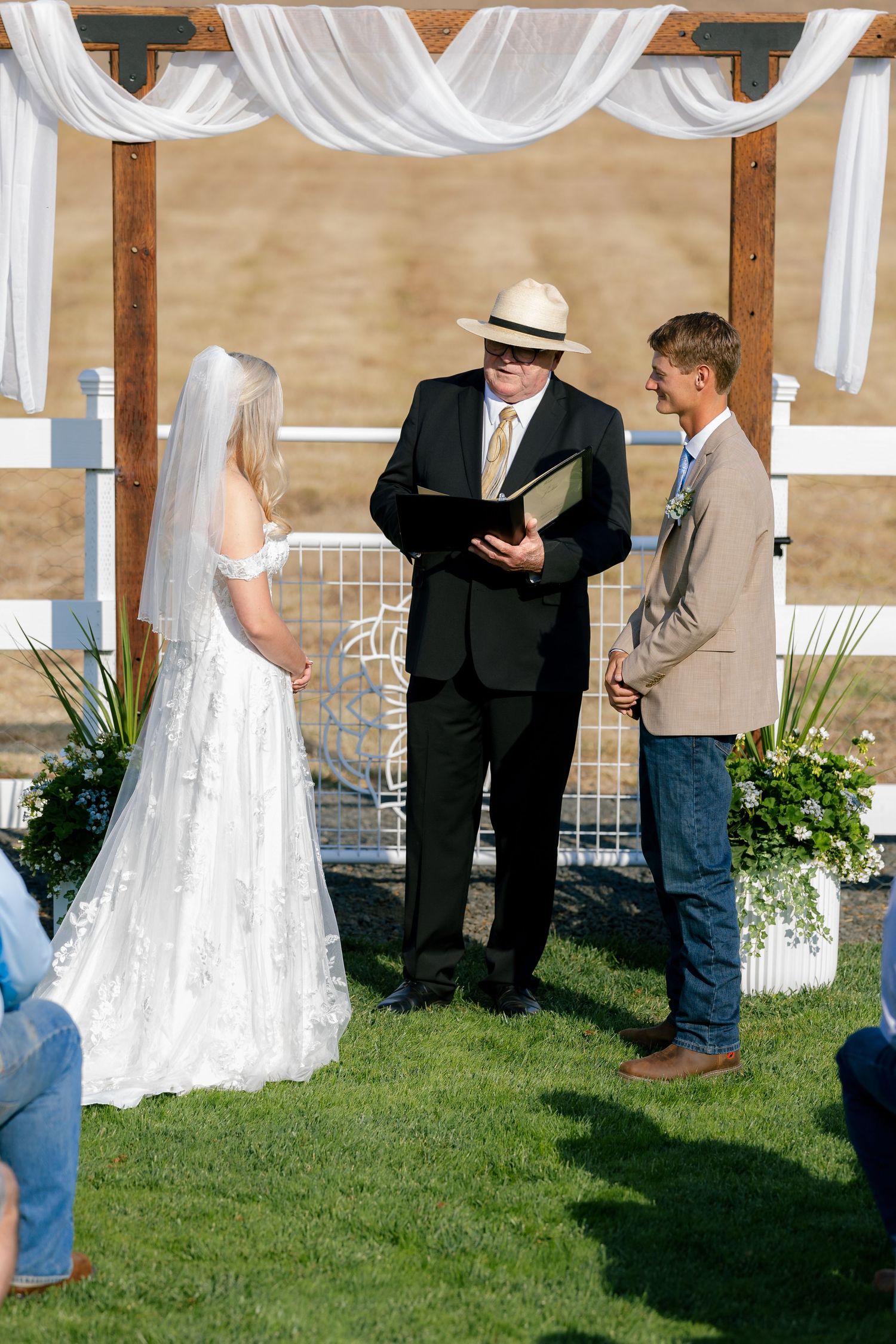 An outdoor wedding ceremony setup with white draping and guests gathered on the lawn.