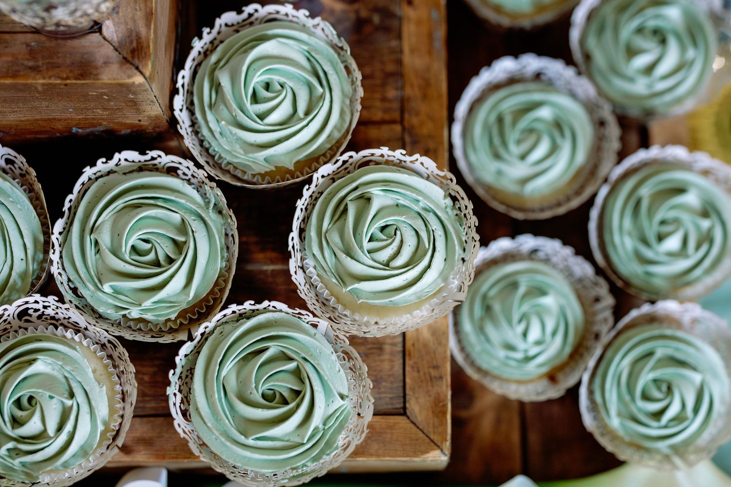 Elegant mint green frosted cupcakes with rose-shaped buttercream swirls arranged in wooden boxes.