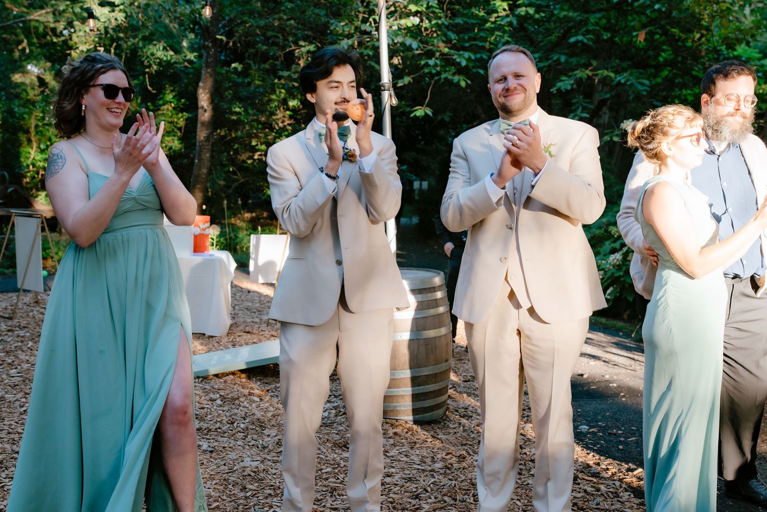 Wedding guests in sage and tan applaud at outdoor garden reception.
