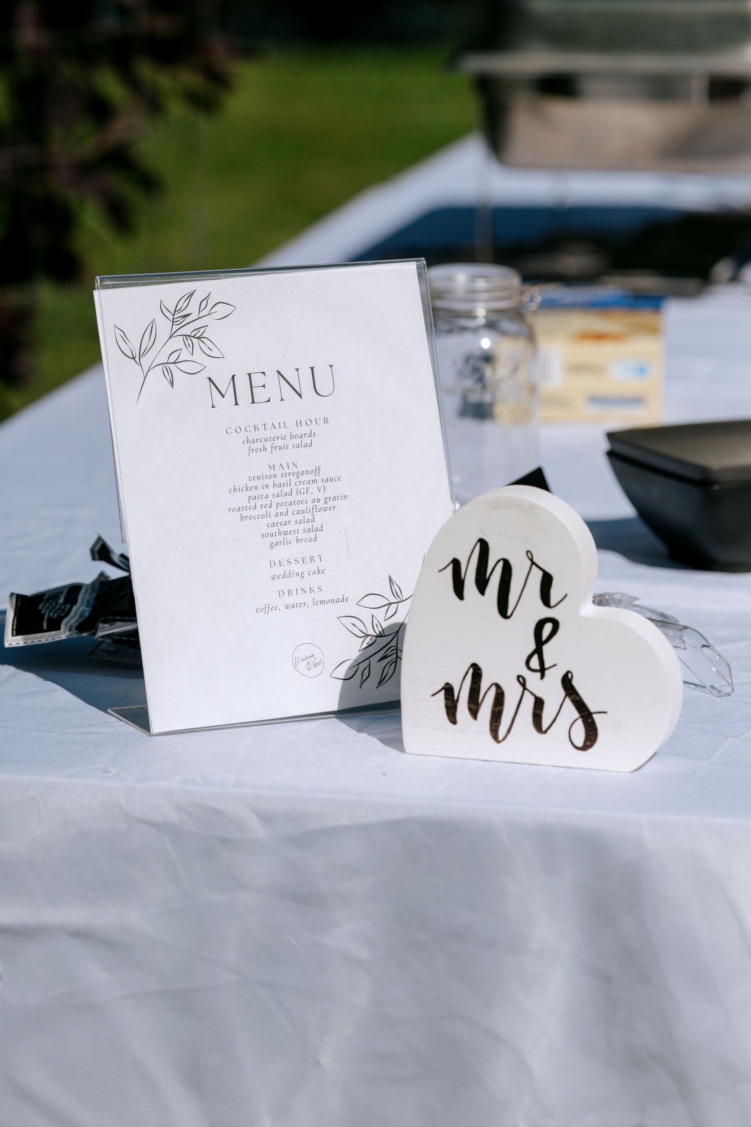 Elegant outdoor wedding table display with menu card and Mr and Mrs heart-shaped sign on white linen.