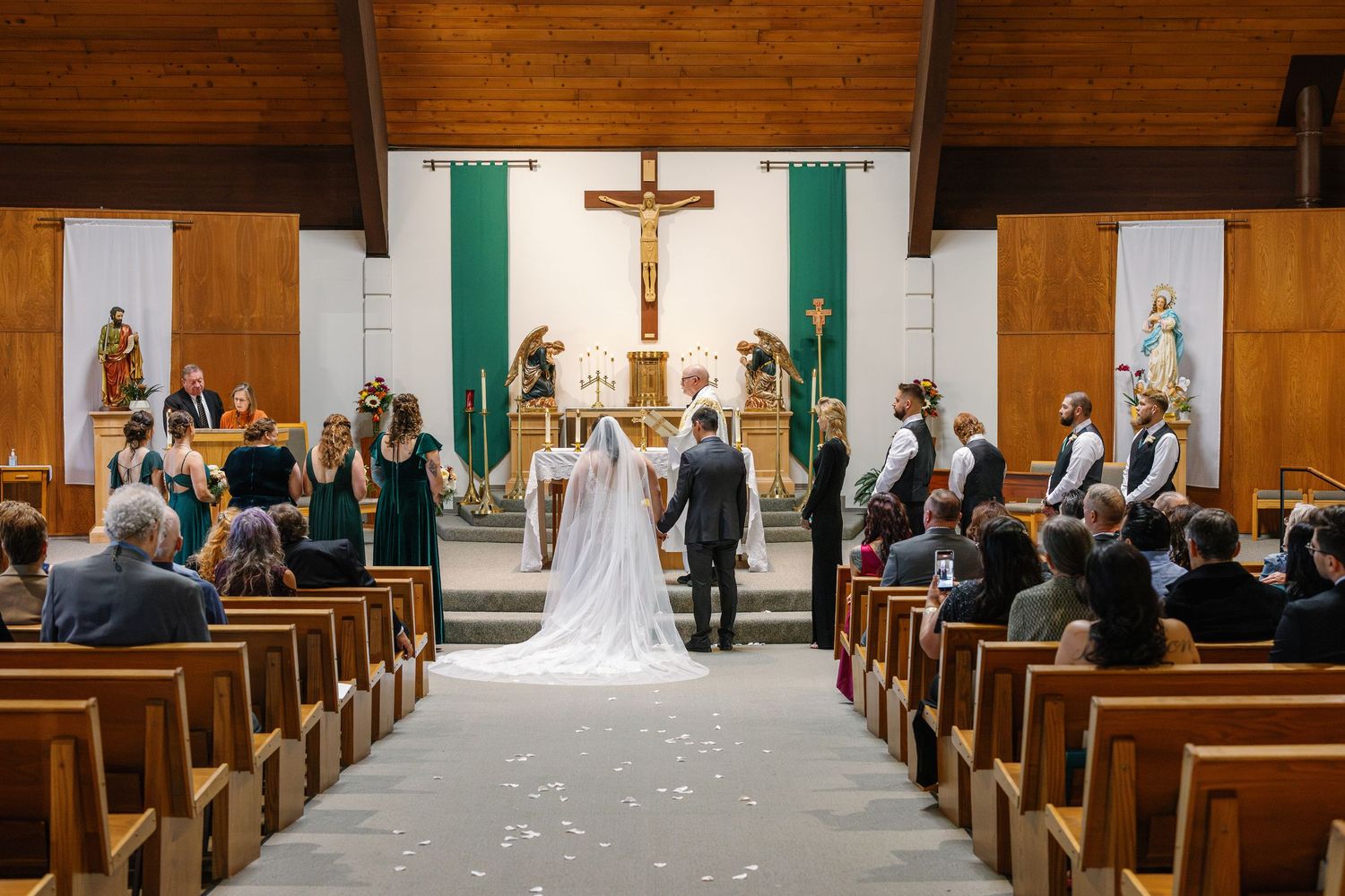 Church interior with wooden pews and cross at altar during wedding ceremony.
