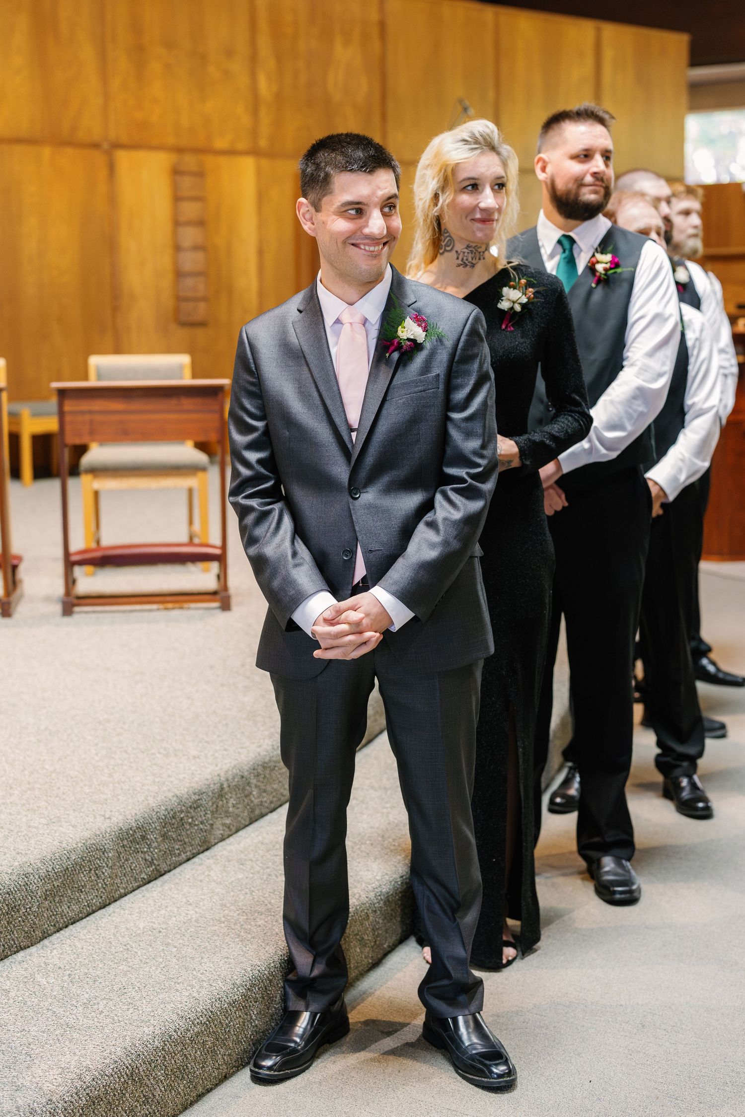 Groomsmen in dark suits line up along carpeted church steps before ceremony.