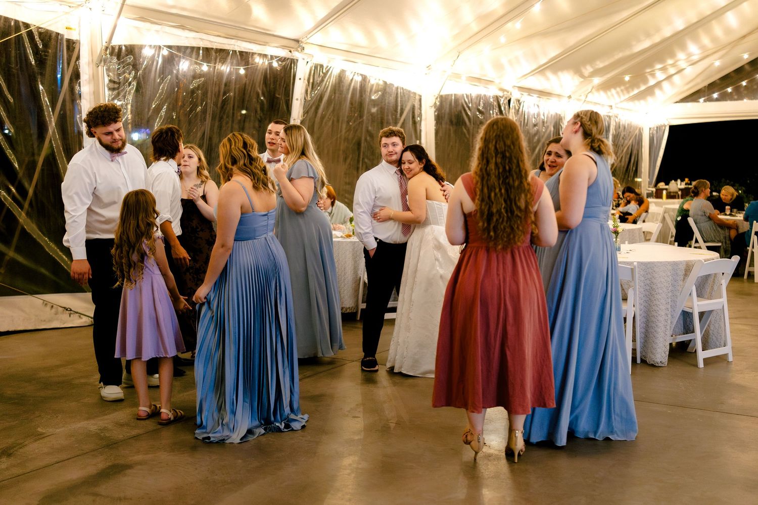 Wedding reception with guests in colorful dresses dancing under illuminated tent.