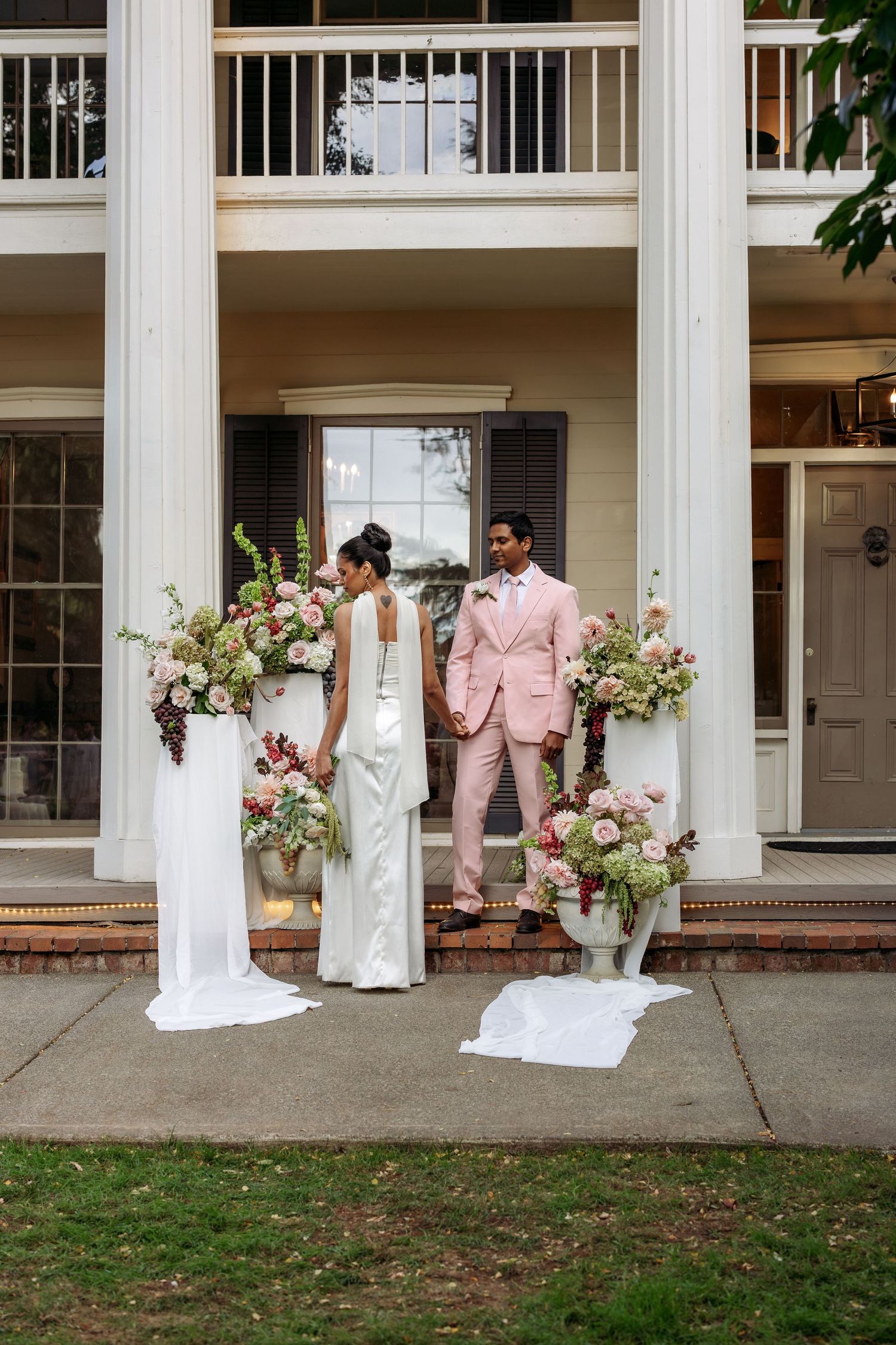 Wedding party posing in front of a classic white columned building with floral arrangements.