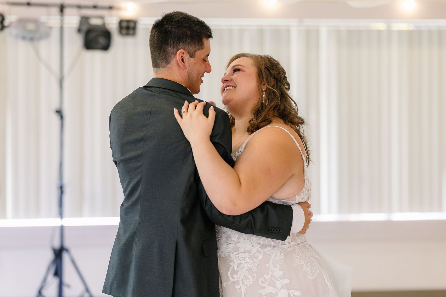Couple shares intimate dance moment at wedding reception with white backdrop.