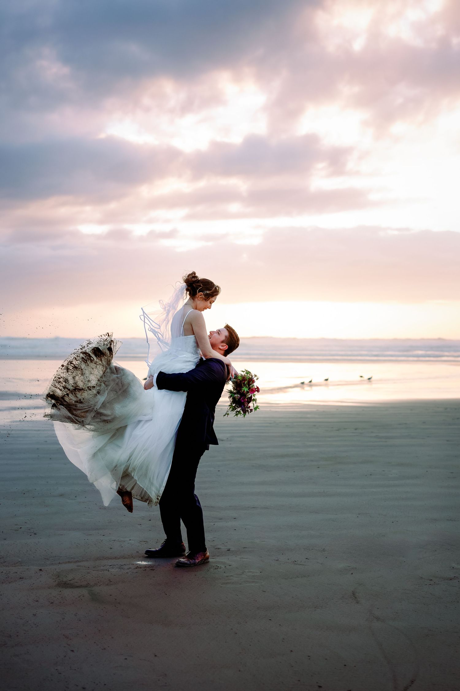 A bride and groom dance playfully on a vast empty beach during golden hour.