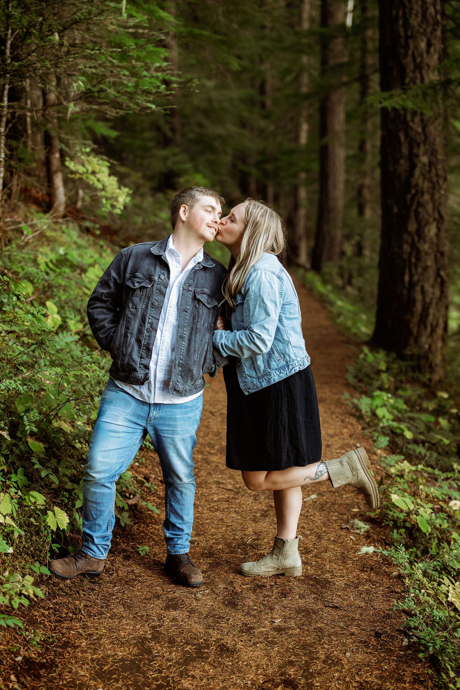 A romantic couple in matching denim outfits share tender moments while walking along a forest trail.