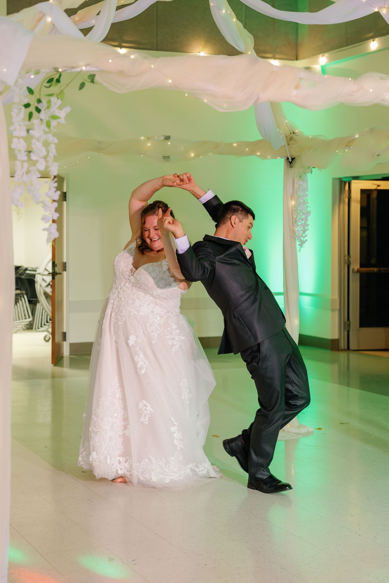 Couple performs playful dance moves under white ceiling decorations with green accent lighting.