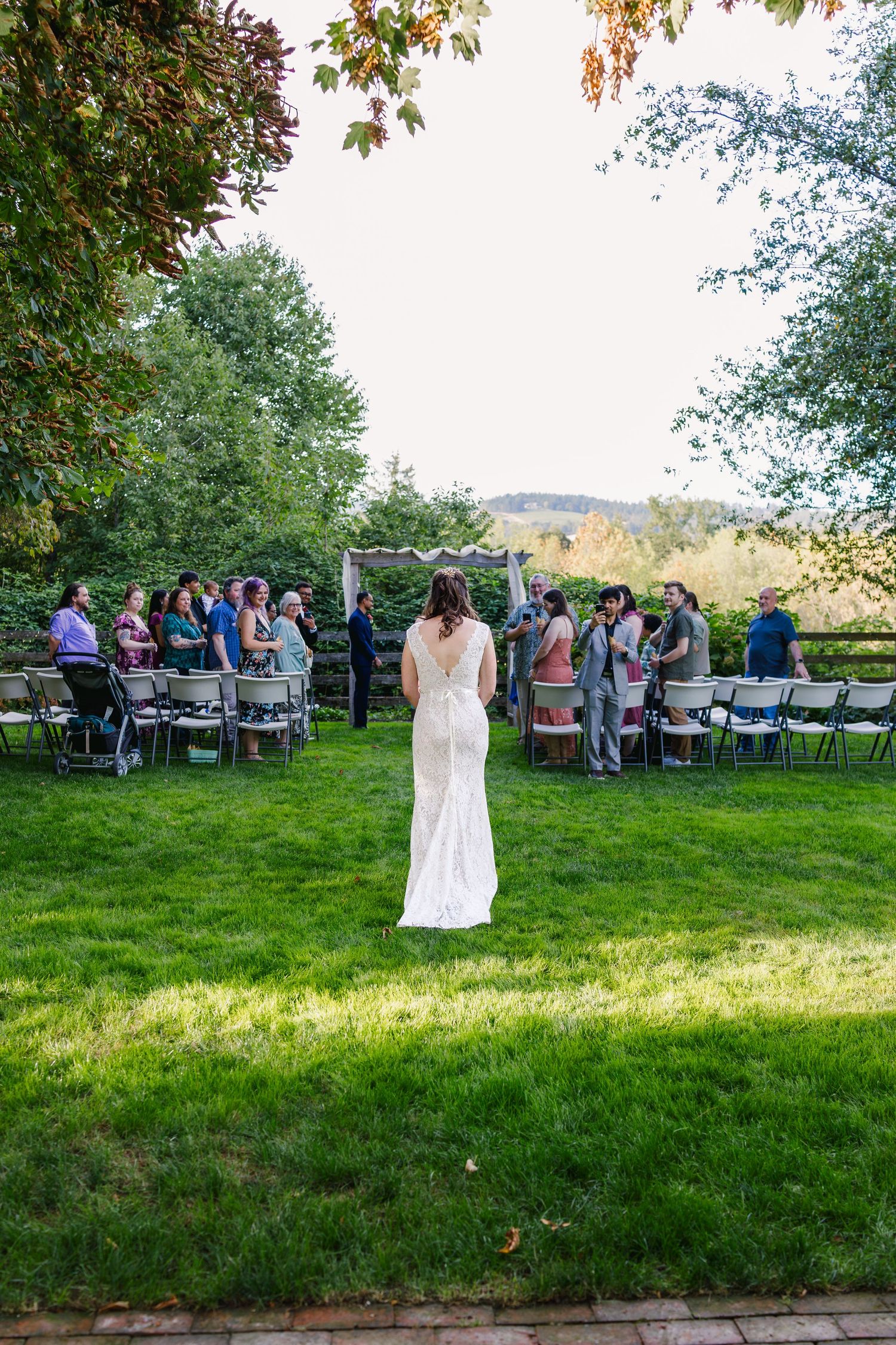 Wedding ceremony setup in a garden with rows of chairs and guests gathered under trees.