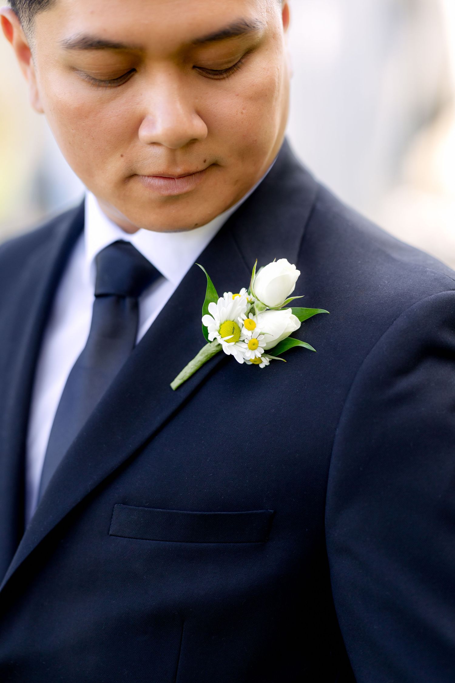 Groom in black suit with white rose boutonniere looking down on his wedding day.
