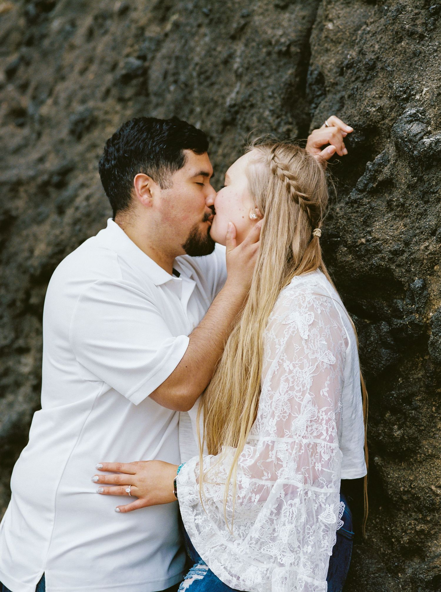Couple sharing a romantic kiss against a dark rocky surface outdoors.