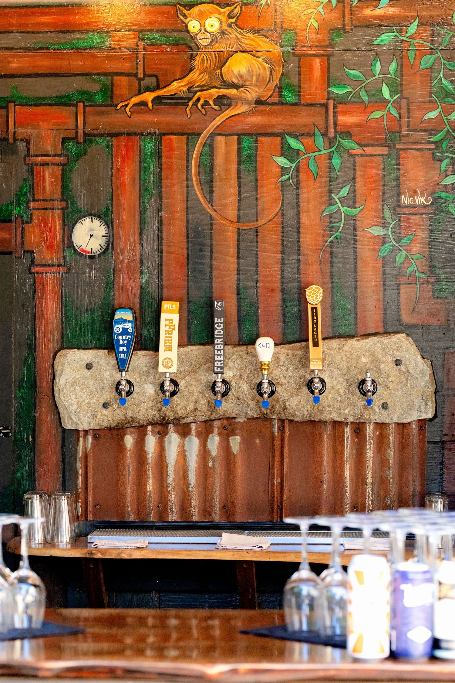 Rustic bar with beer taps mounted on stone slab and colorful monkey mural.