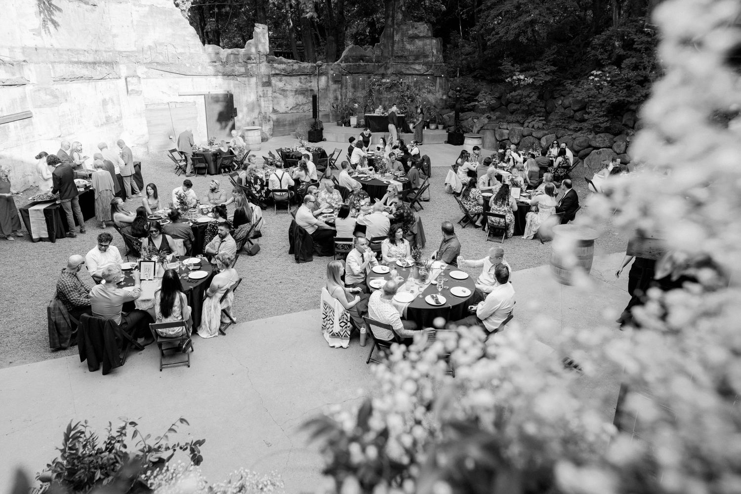 Aerial black and white photo of wedding reception guests seated at round tables in an elegant outdoor courtyard.