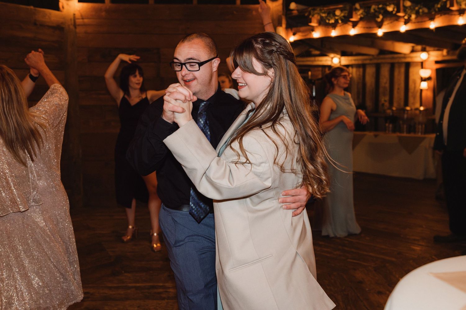 Couple shares a romantic dance at a rustic wedding reception venue with warm ambient lighting.