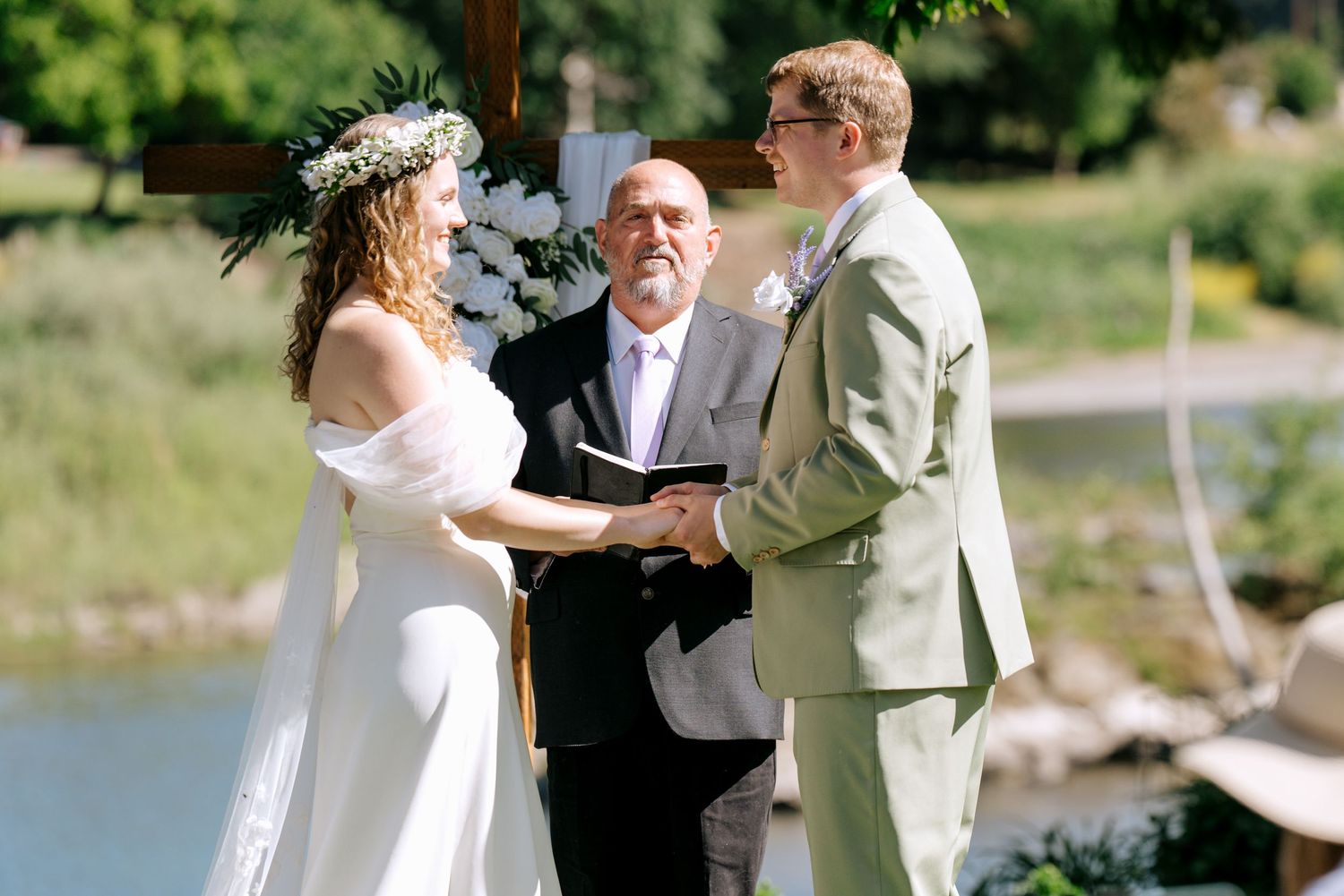Bride and groom exchange vows outdoors with officiant by a serene lakeside wedding ceremony.