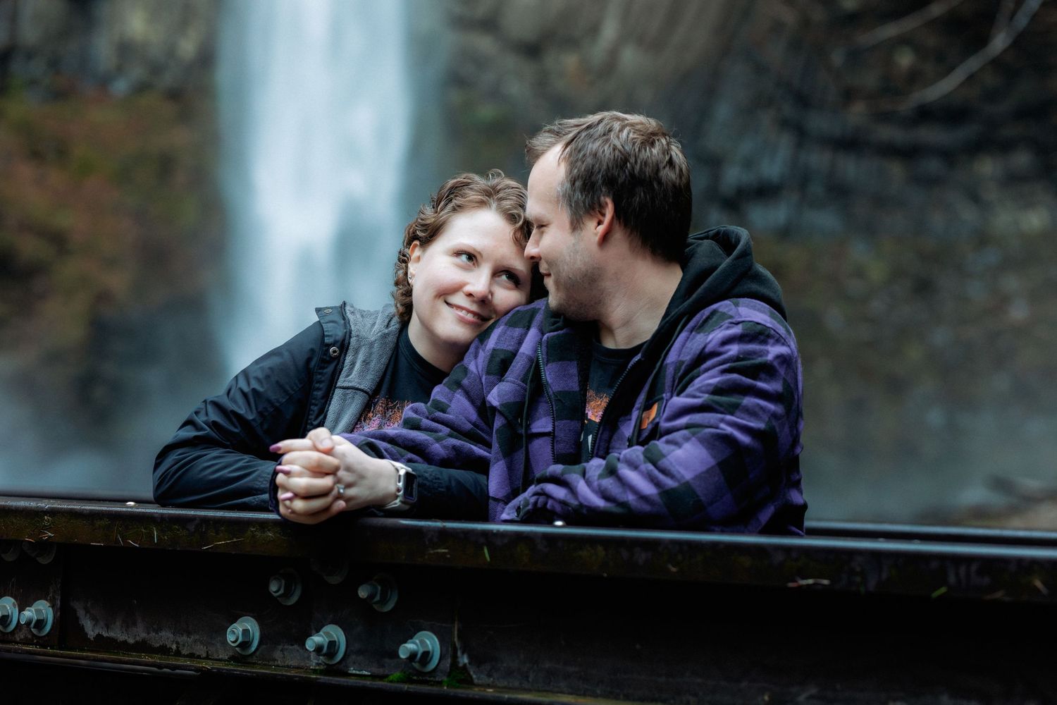 A romantic couple shares an intimate moment together while sitting outdoors against a scenic natural backdrop.