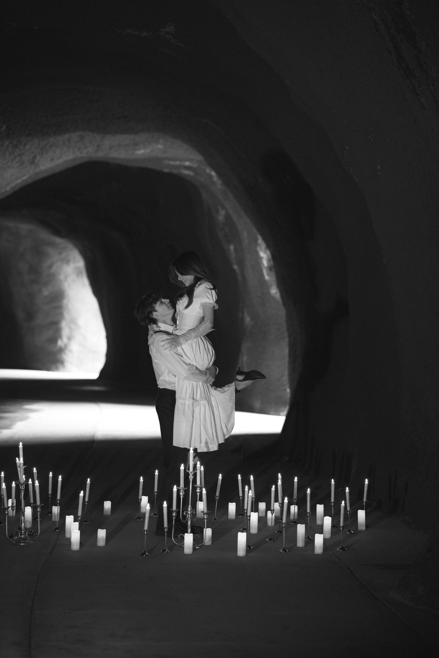 Silhouettes of people standing in a dimly lit tunnel with rows of glowing candles creating a mystical ambiance.