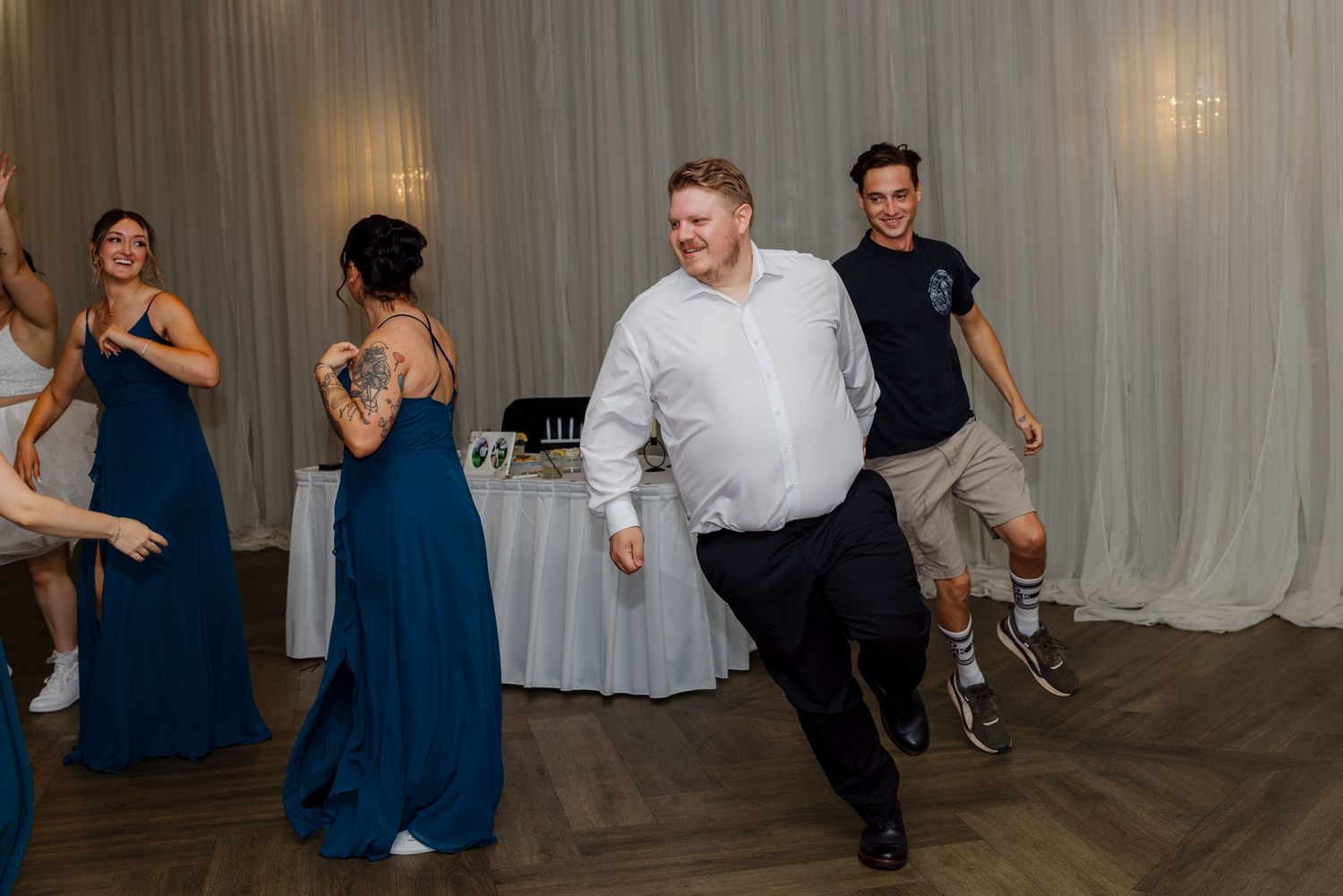 Guests dancing joyfully at a wedding reception in a decorated venue with blue bridesmaid dresses.