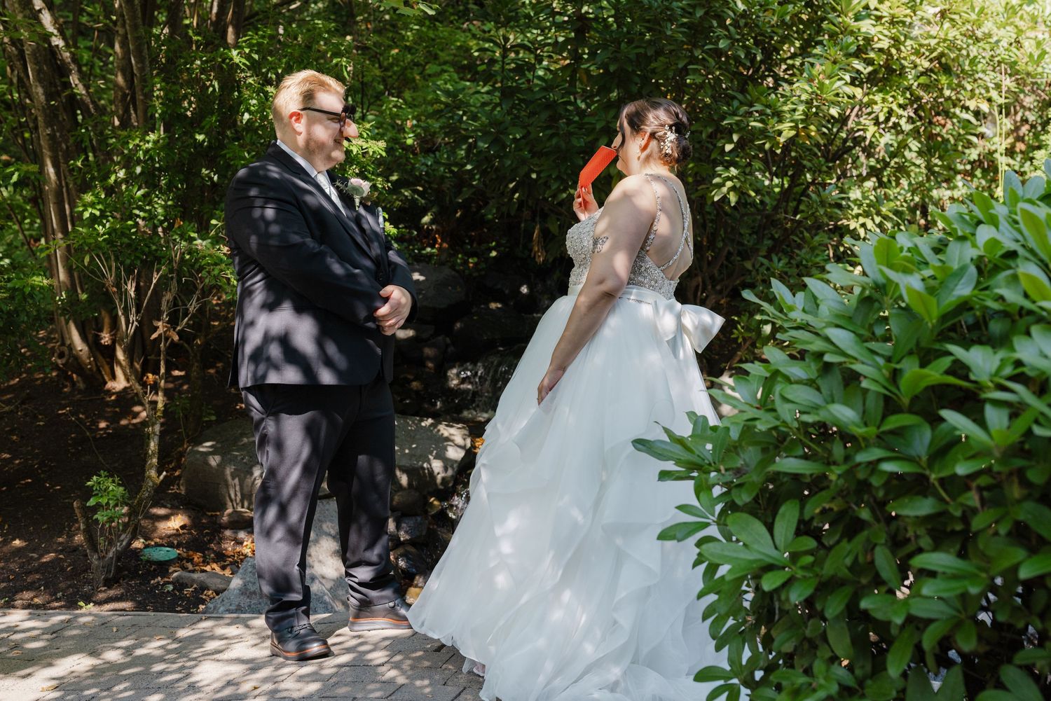 Groom awaits his bride during an outdoor first look moment surrounded by green trees.