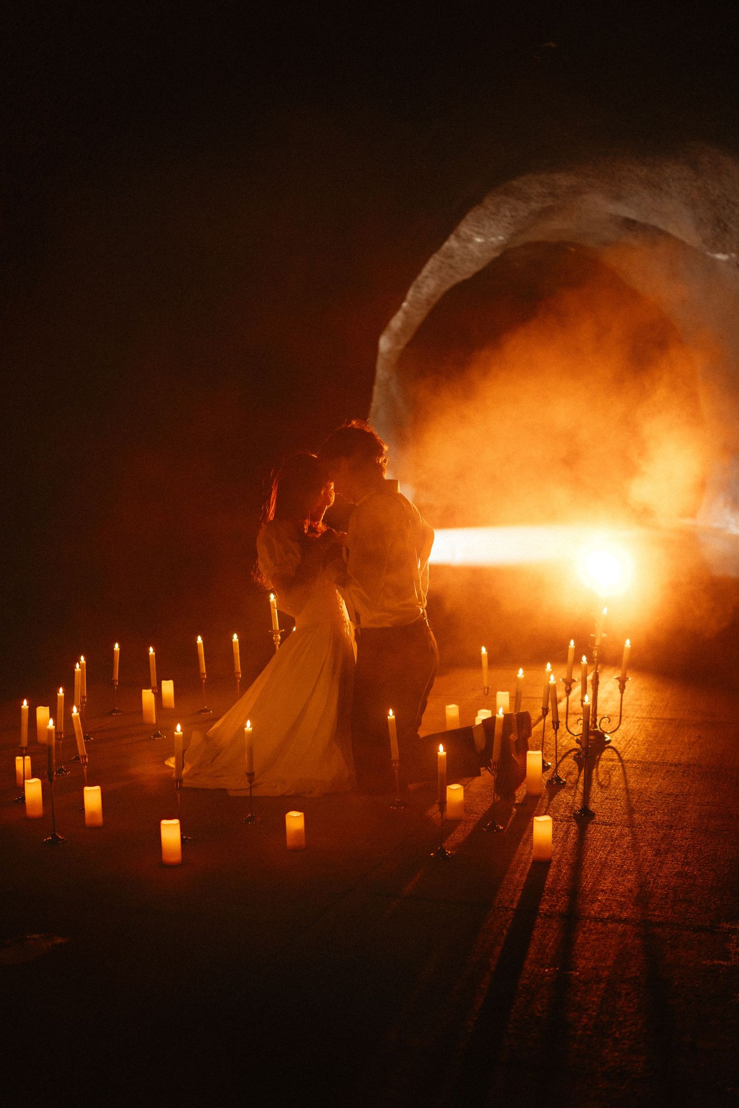 Silhouettes move through a candlelit outdoor setting creating dramatic shadows and light.