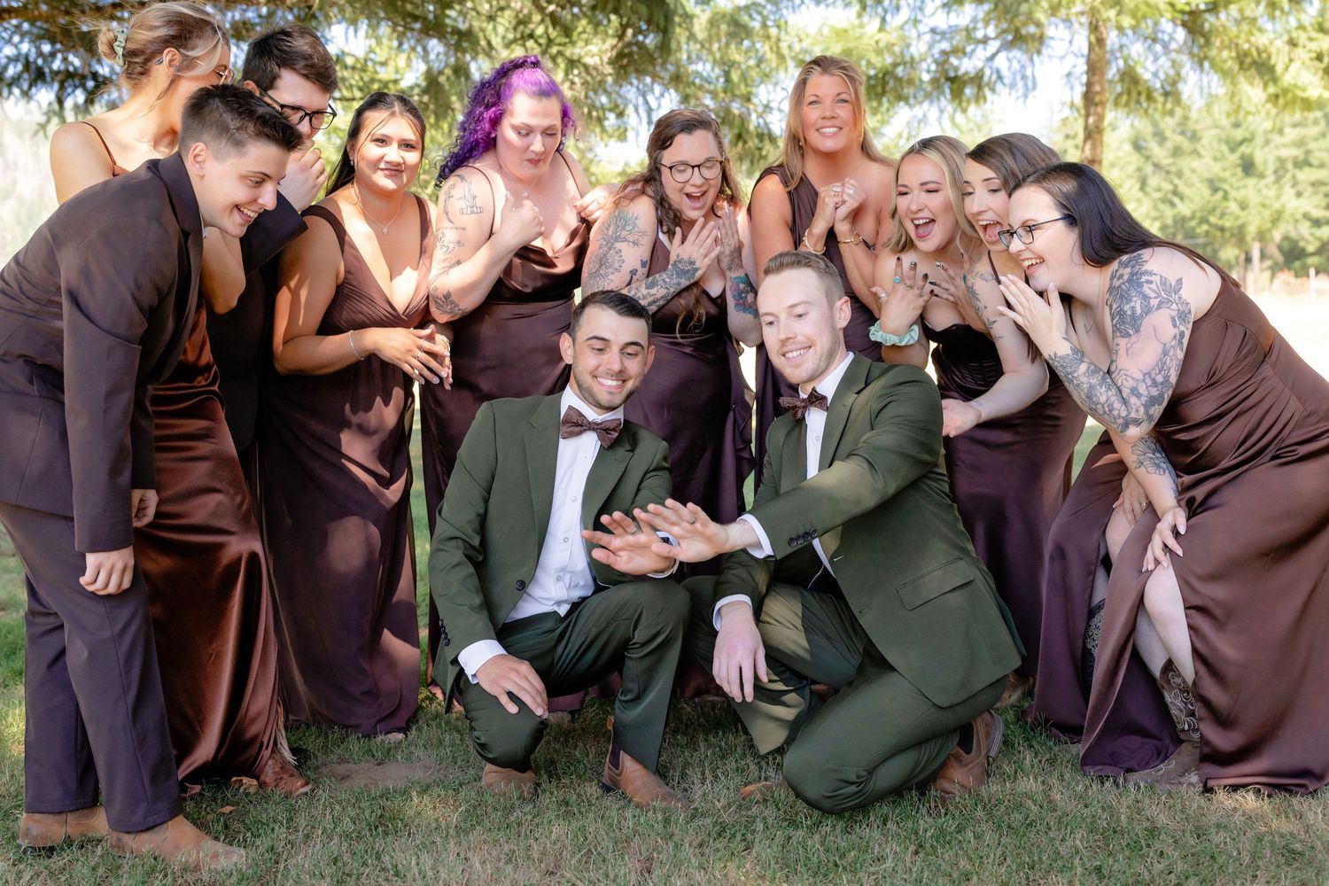Two grooms surrounded by bridesmaids in brown dresses laughing together during outdoor wedding party photos.
