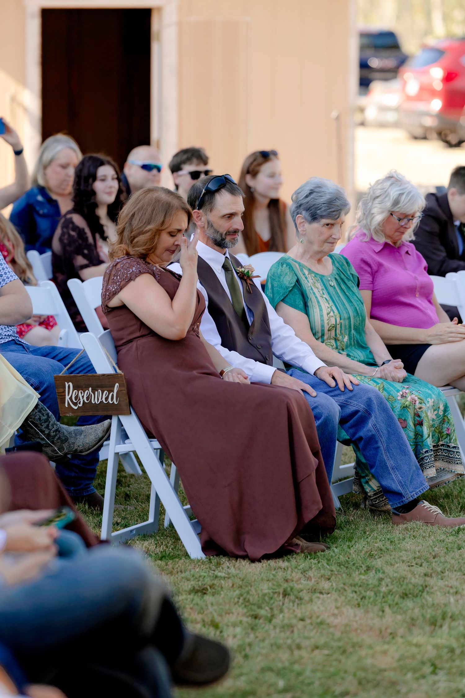 Guests seated in white chairs at an outdoor wedding ceremony, with a reserved sign on the front row.