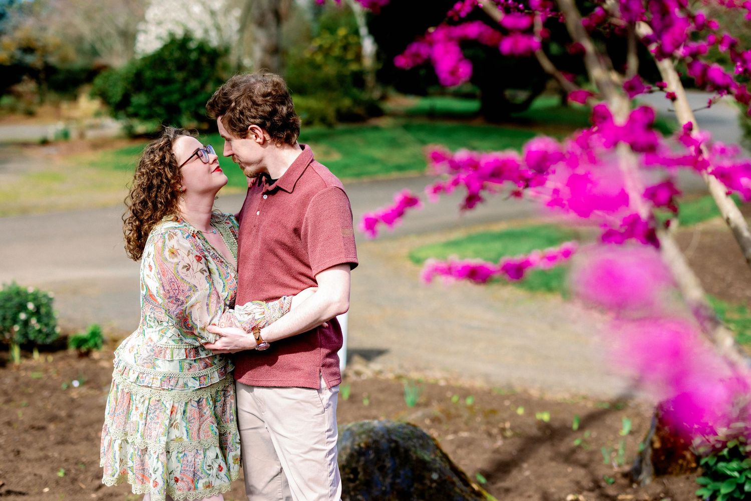 A couple shares a romantic moment in a garden with vibrant pink flowers falling around them.