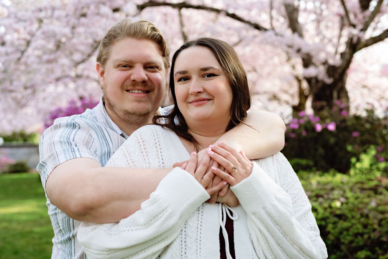 A couple embraces outdoors during spring with cherry blossoms blooming in the background.
