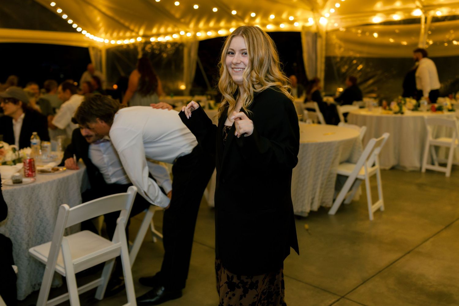 Guests enjoying an evening wedding reception under warm glowing lights in an elegant tent venue.