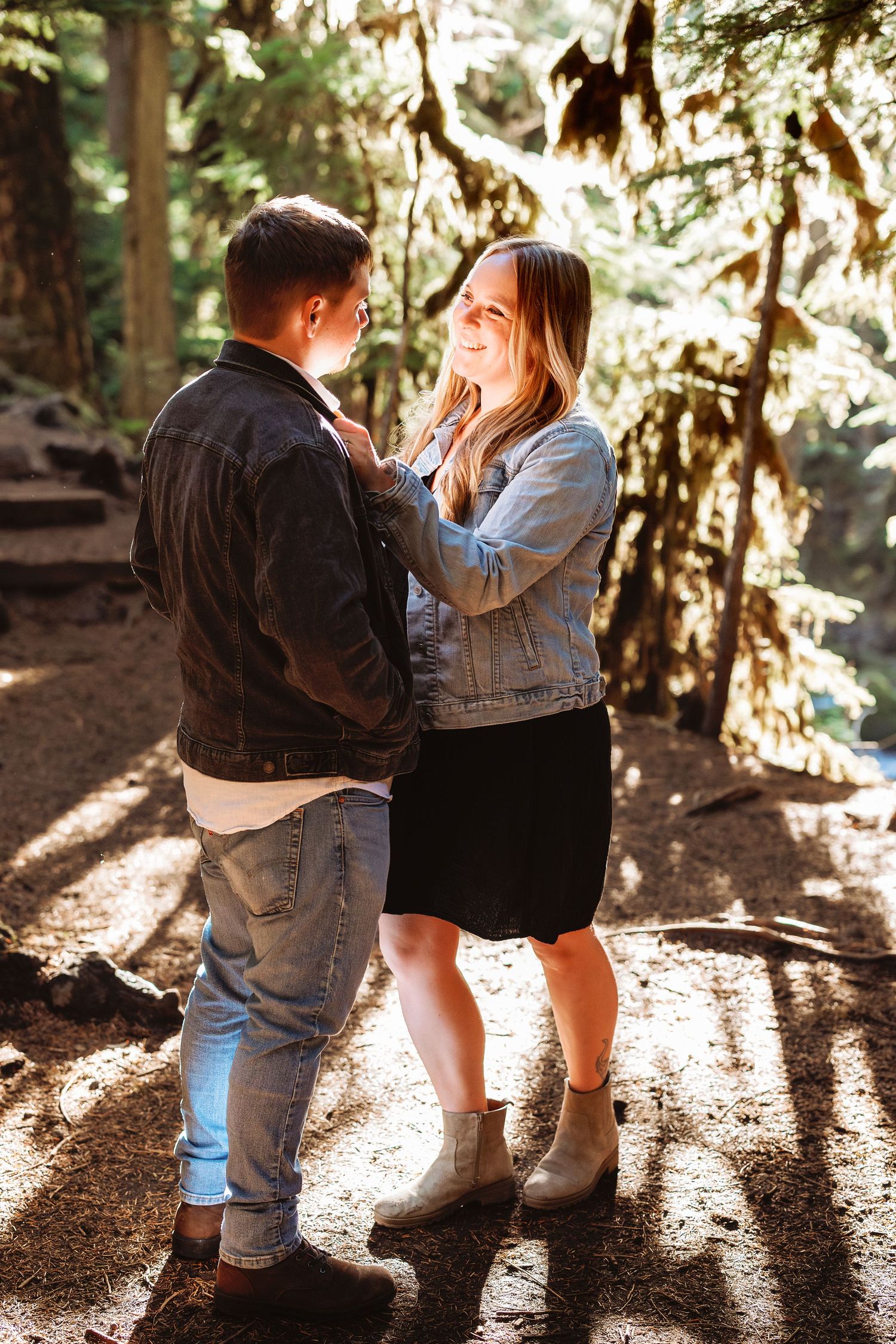 A couple shares an intimate moment in a sunlit forest setting, creating romantic silhouettes among the trees.