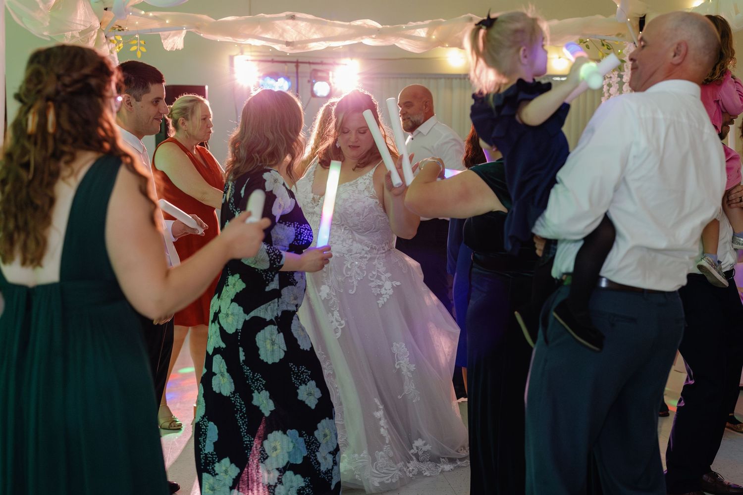 Wedding guests dancing and celebrating at a reception with colorful lighting.