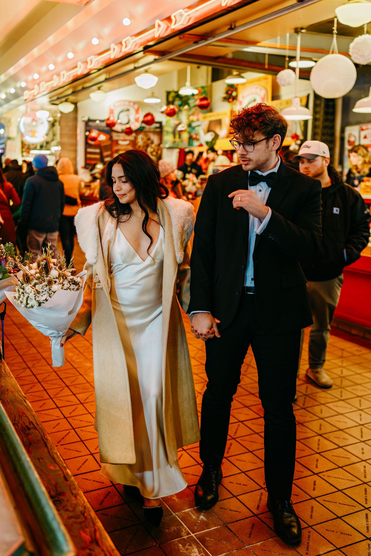 Wedding party walking through a tiled indoor venue with decorative lighting overhead.