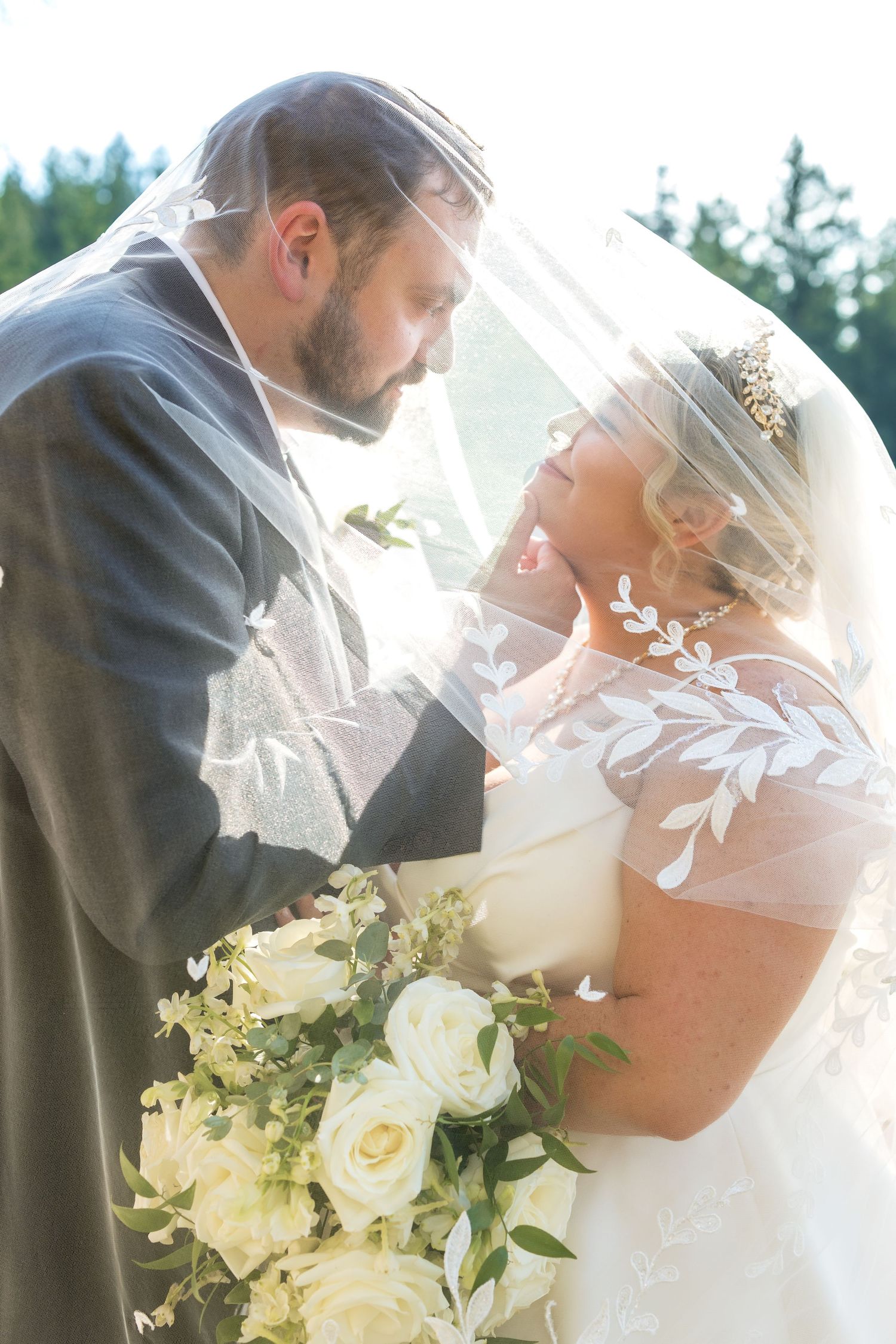 A romantic wedding moment captured through a veil with white roses and sunlit glow.
