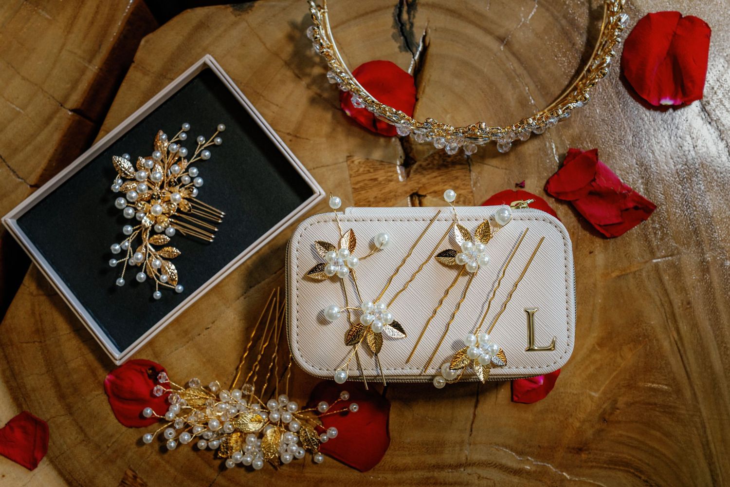 Elegant bridal accessories including pearl hair combs, floral headpiece, and white clutch displayed with red rose petals.
