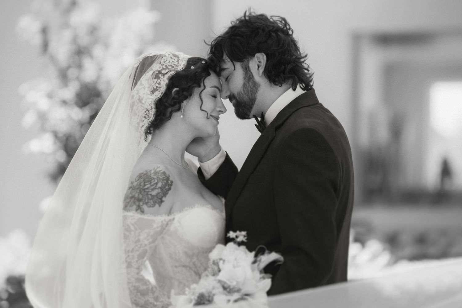 Black and white wedding photo of bride and groom sharing an intimate moment at the altar.