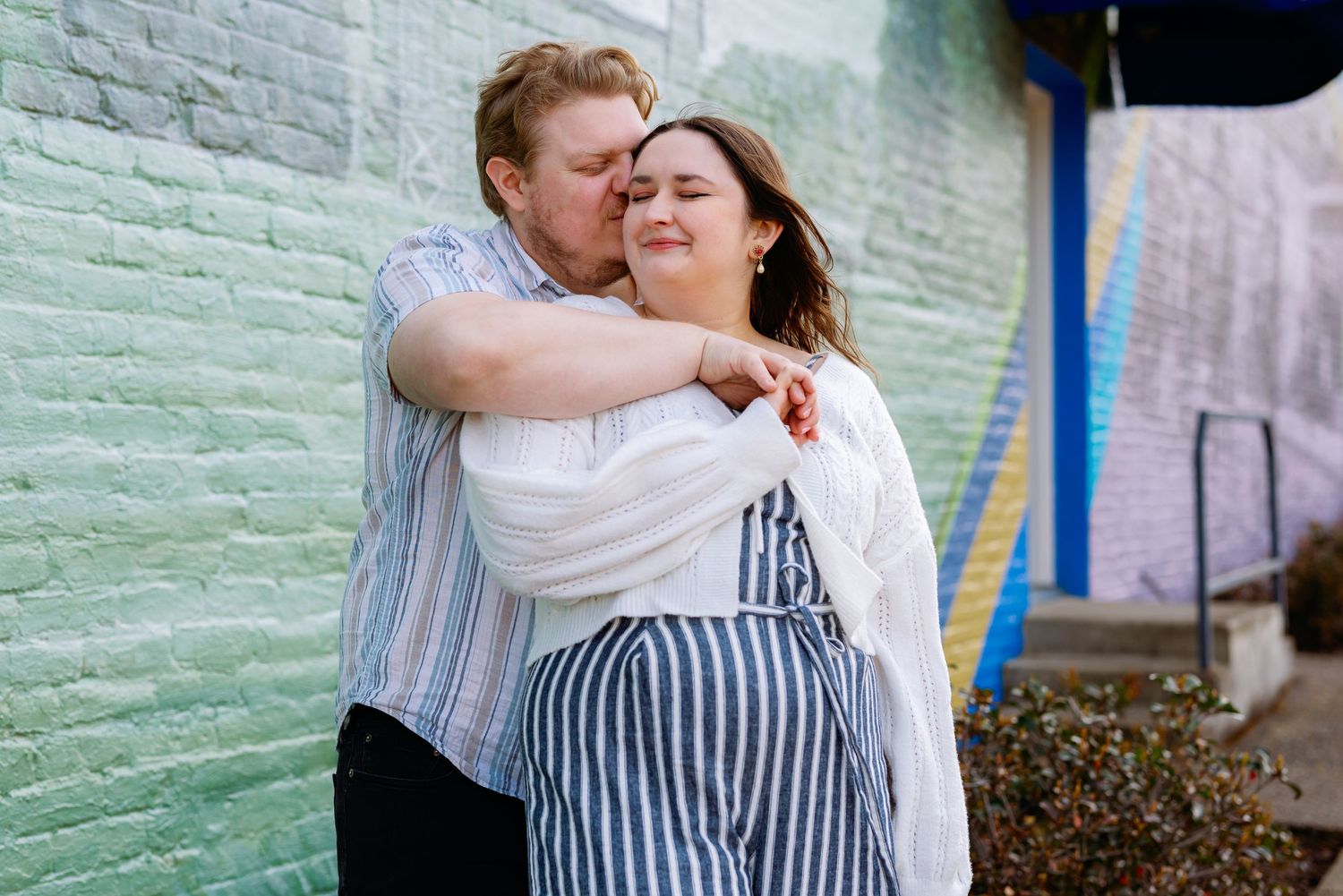 Romantic couple embracing against pastel painted wall outdoors.