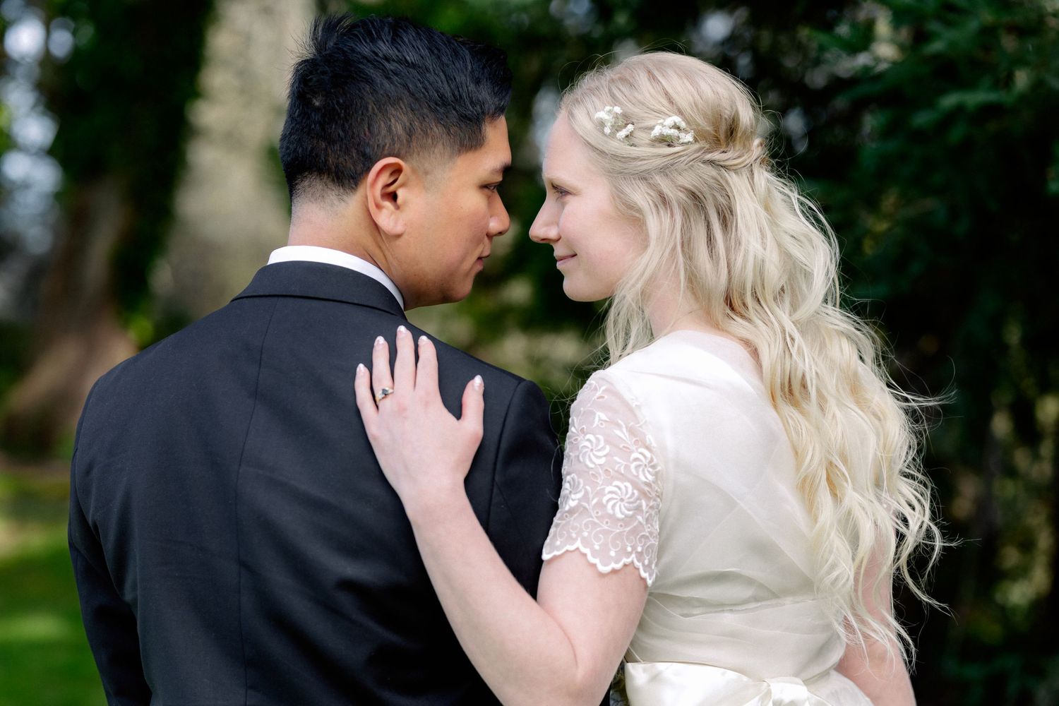 Bride and groom share a romantic moment gazing at each other in a lush green garden.
