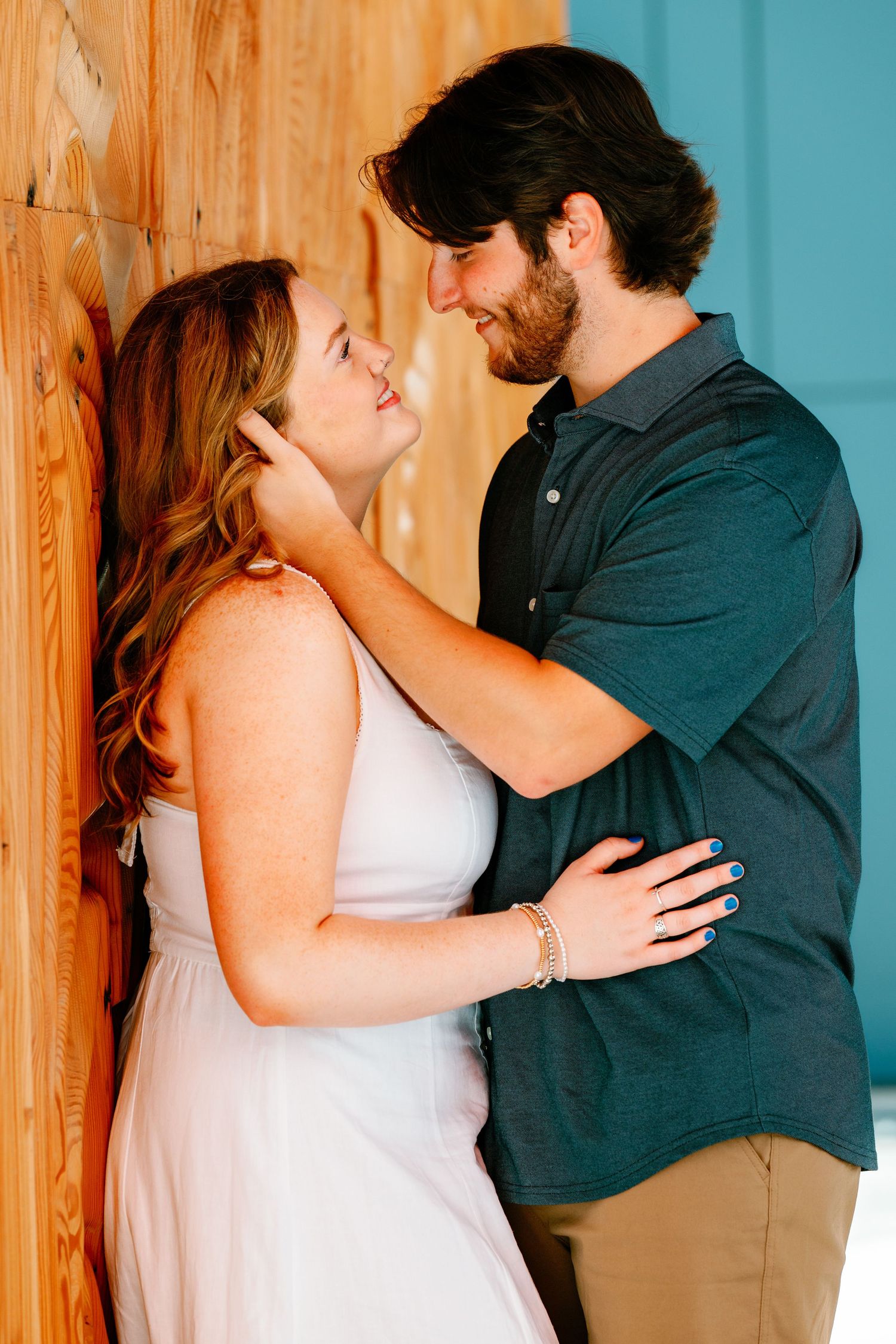 A couple shares a romantic moment leaning against a wooden wall, the man tenderly touching the woman's face.