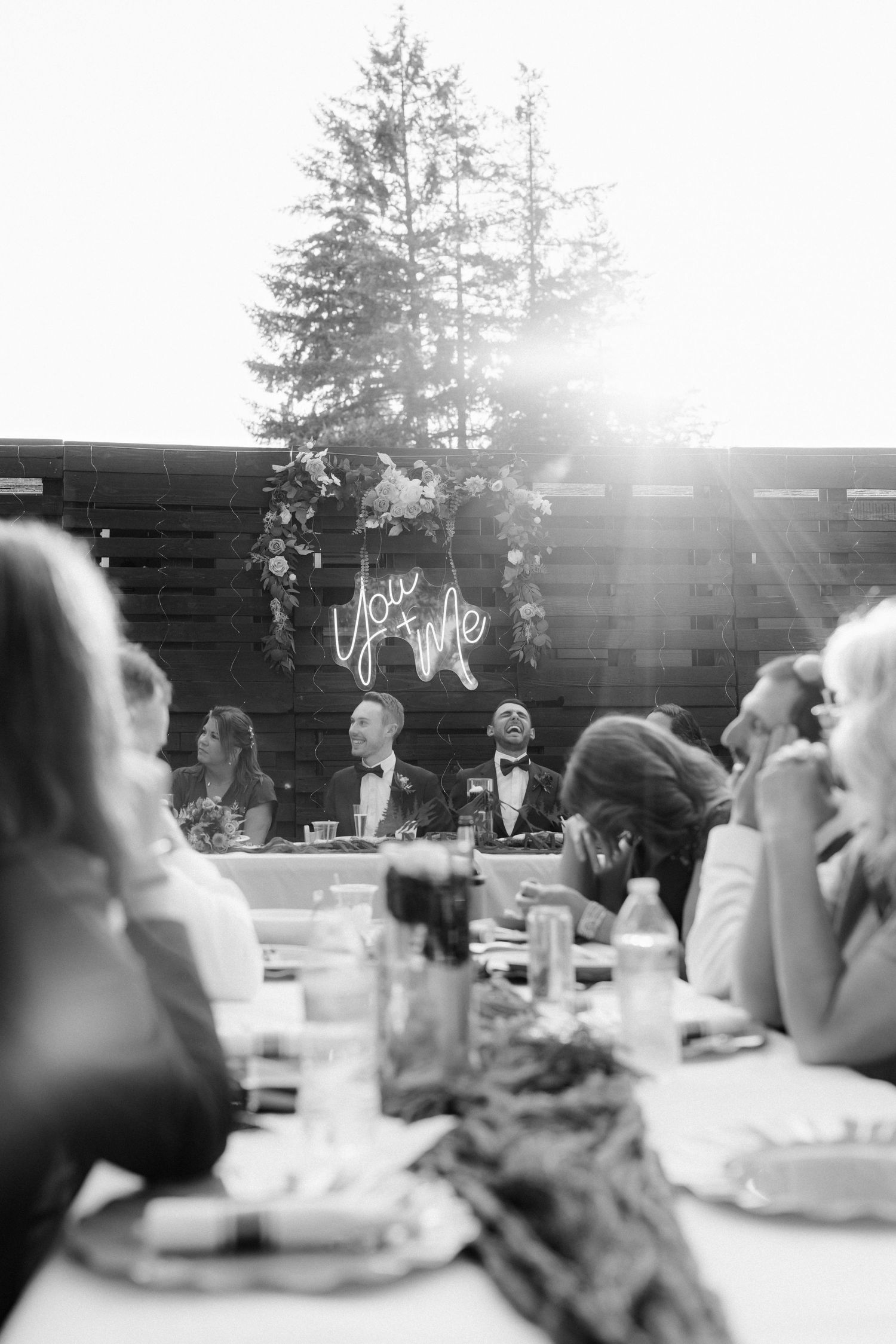 Black and white photo of wedding couple at head table with neon sign glowing behind them.