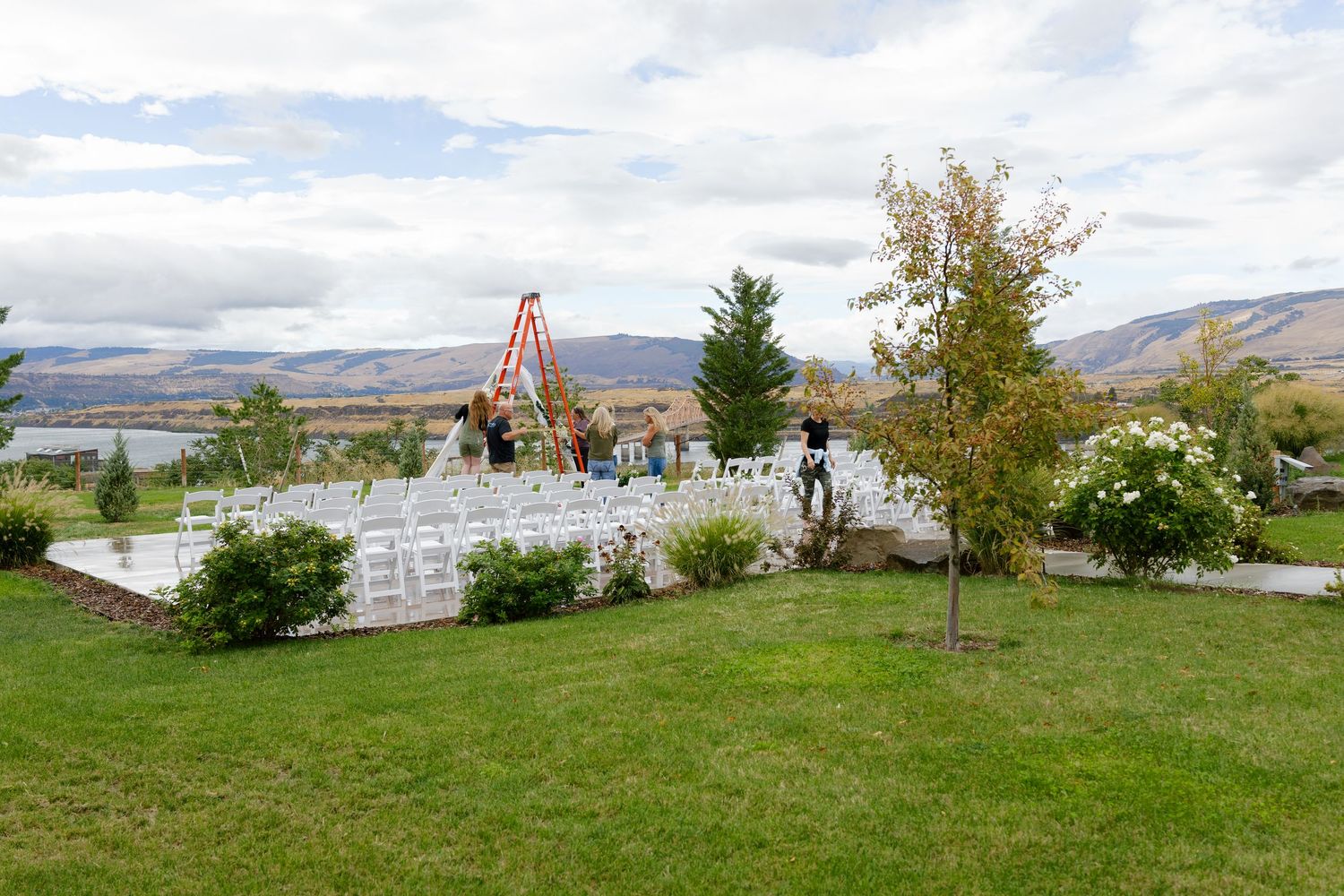Panoramic view of an outdoor wedding venue with white chairs and orange arch against rolling hills.