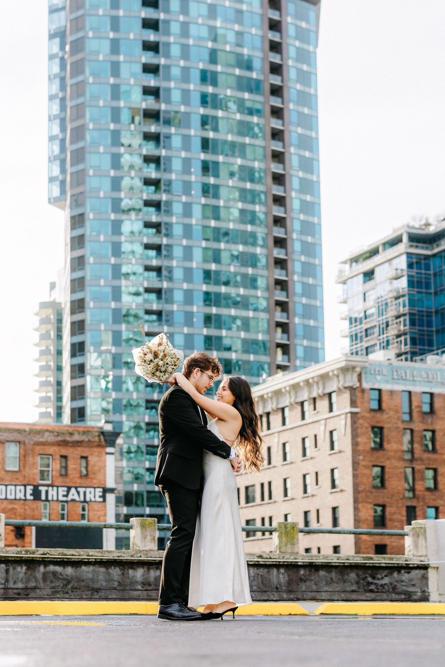 Dancing couple on rooftop with glass skyscraper and brick building backdrop.