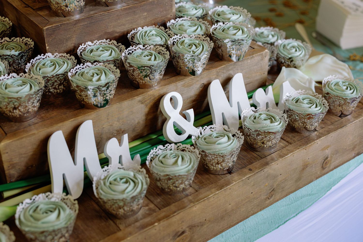 Rustic wooden plank displays rows of green frosted cupcakes alongside white decorative letters for event styling.
