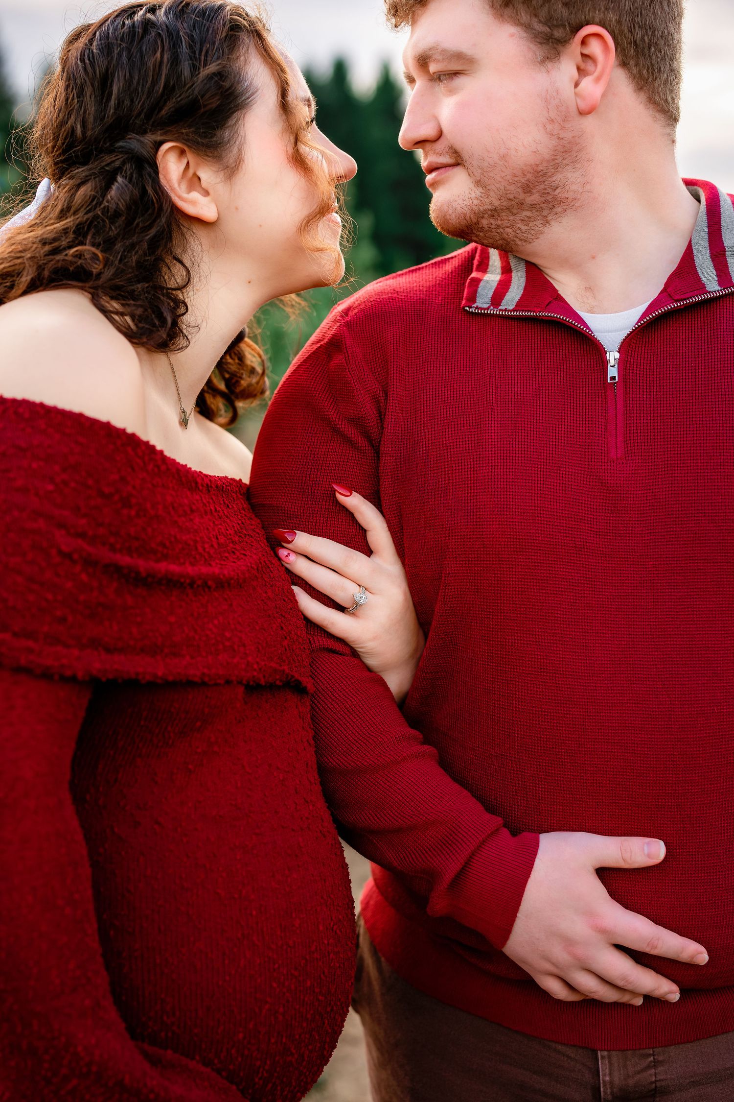 A couple in red sweaters share an intimate moment during an outdoor photo session.