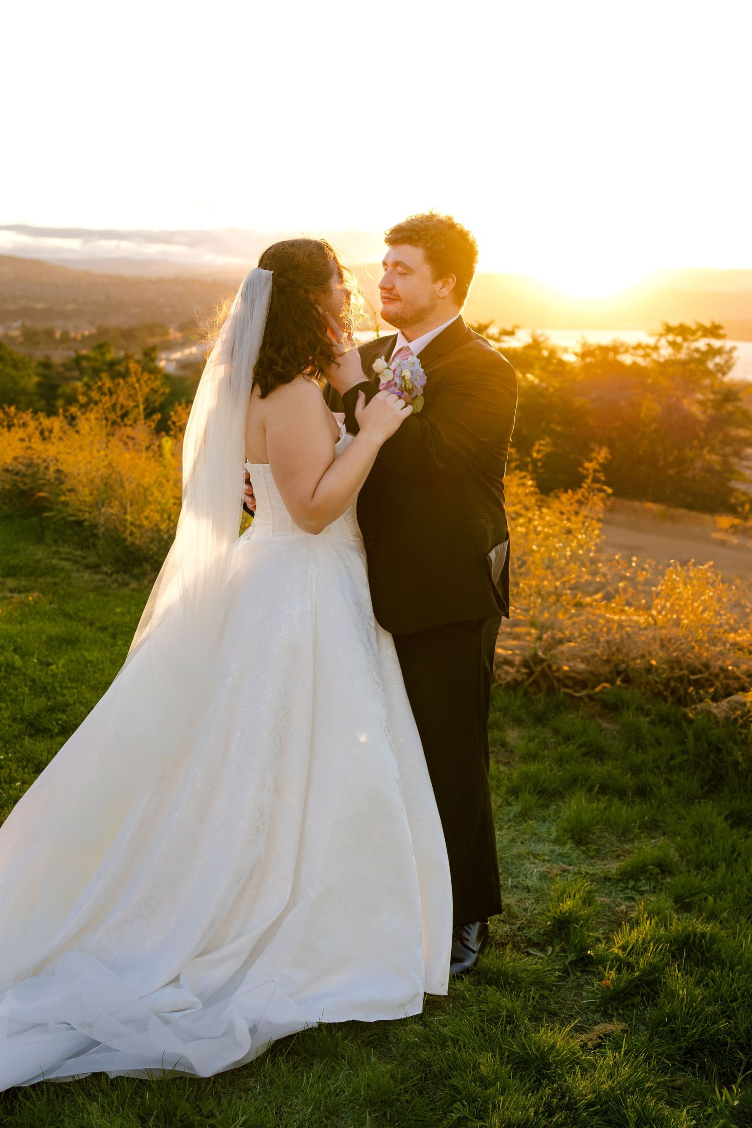 Romantic sunset portrait of newlyweds on a grassy hillside with bride's dress flowing in the breeze.