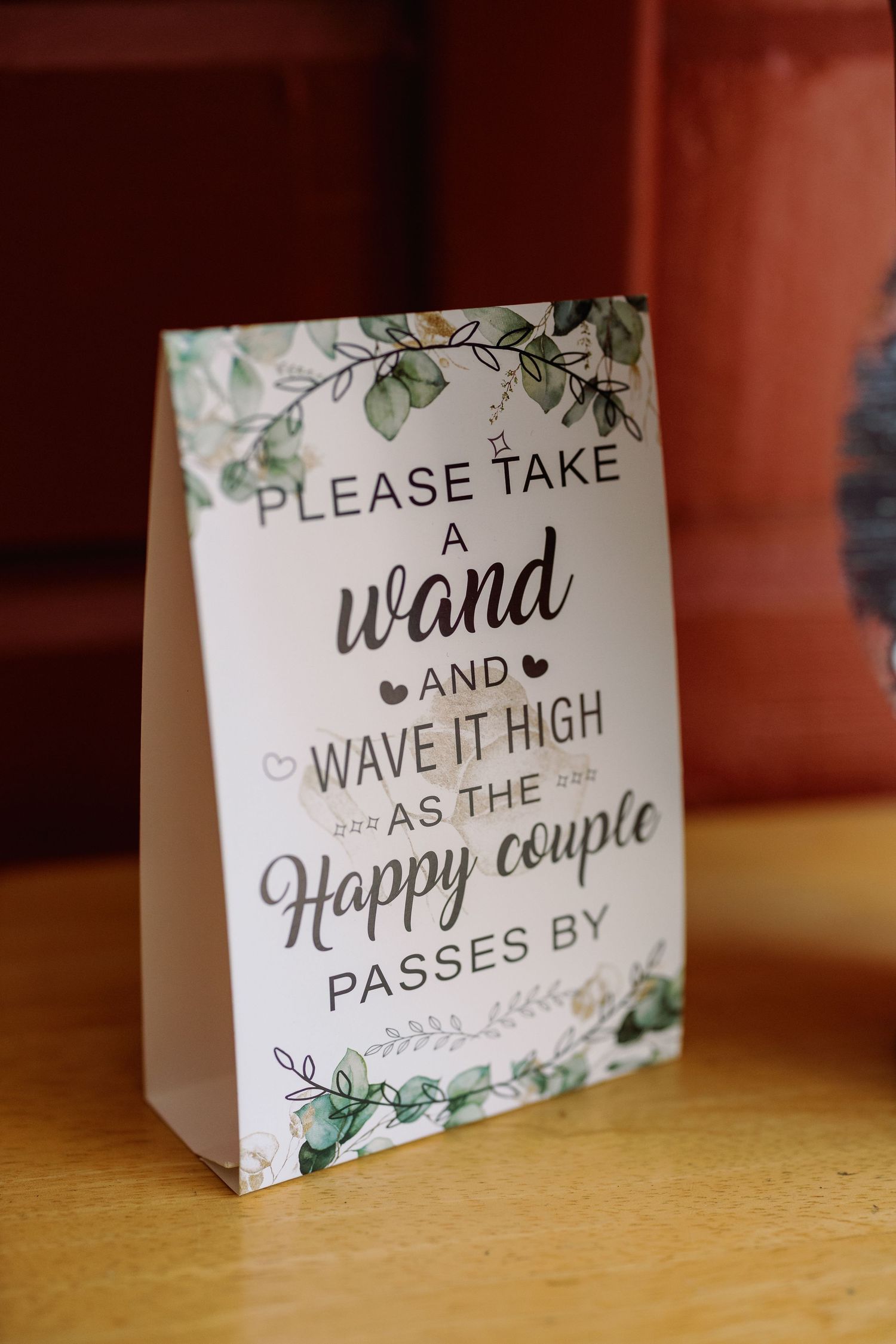 Wedding sign reading 'Please take a wand and wave it high as the happy couple passes by' with floral design.