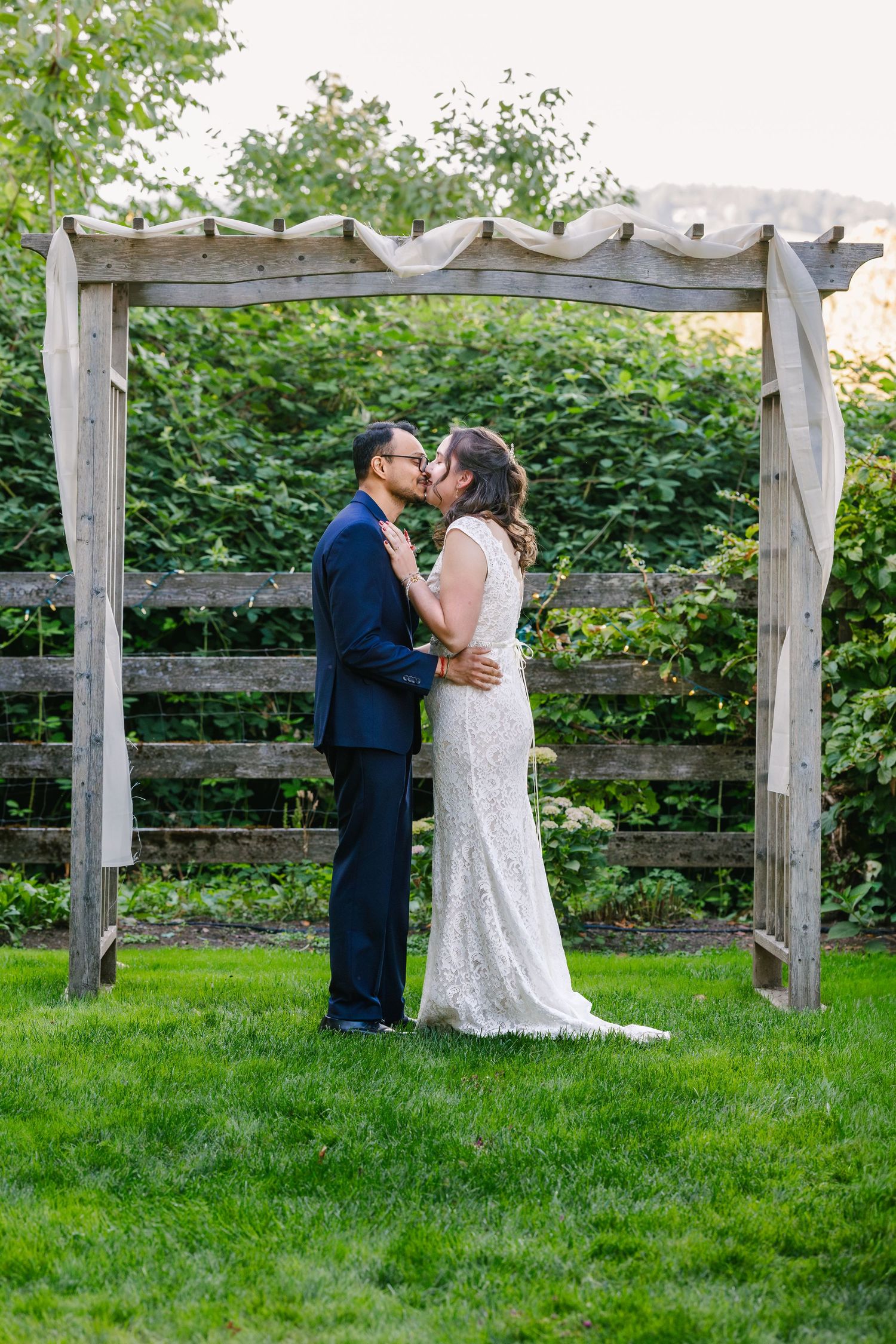 A romantic wedding couple shares intimate moments in a garden setting with a rustic wooden fence backdrop.