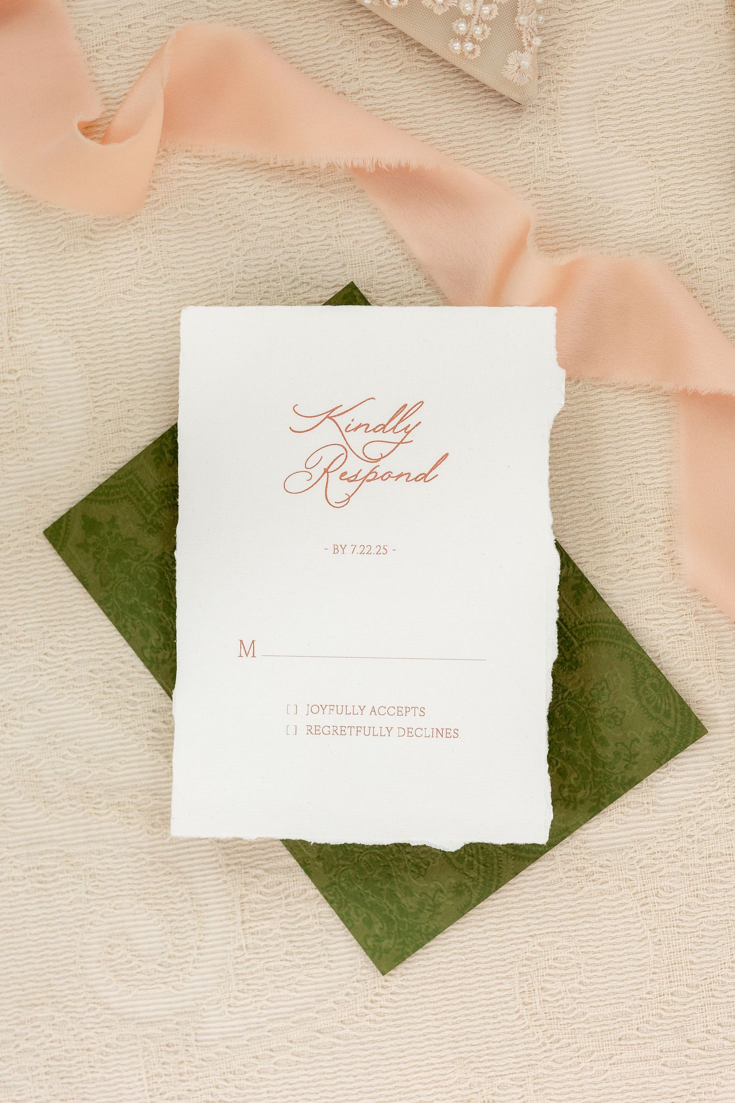 Wedding invitation suite with blush pink ribbons and green accents on a textured cream background.