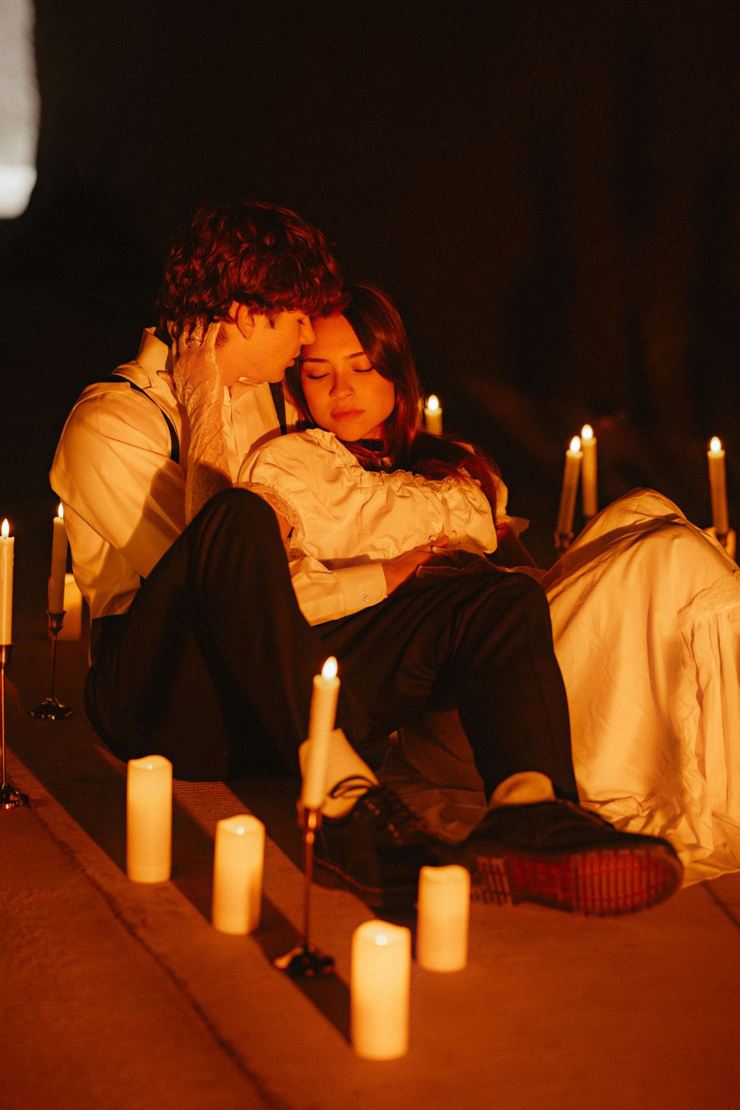 A couple rests intimately among candlelight in warm orange tones.