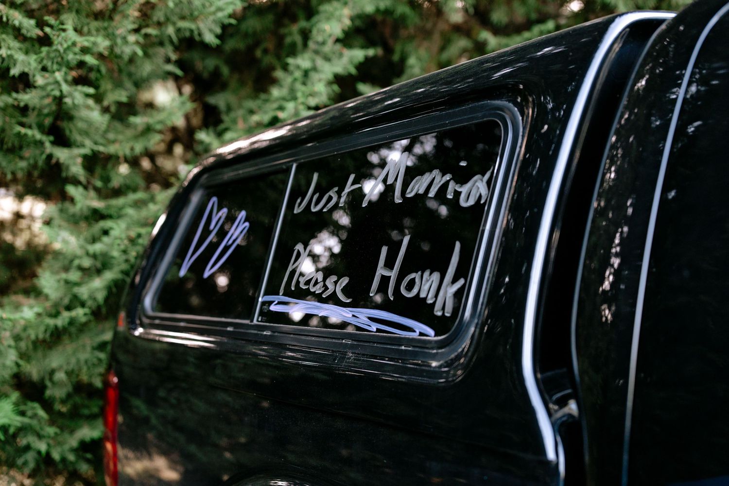Black truck rear window with Just Married Please Honk written in white letters after wedding.